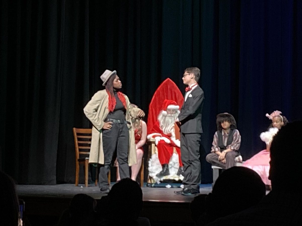 After the murder of the Mysterious Host, the Re-enacted Mysterious Host, played by Alley Saenz, 9, investigates the Pompus Millionaire, played by Omar Ruiz , 9. 